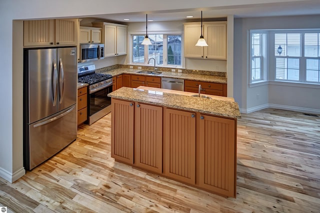 kitchen with sink, stainless steel appliances, hanging light fixtures, and an island with sink