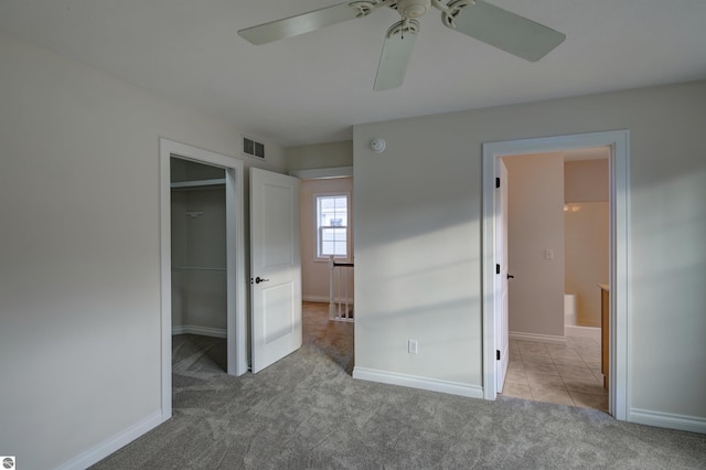 unfurnished bedroom featuring ceiling fan, a walk in closet, light carpet, and a closet