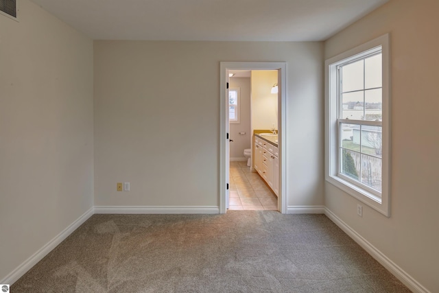 unfurnished bedroom featuring multiple windows, ensuite bathroom, and light carpet