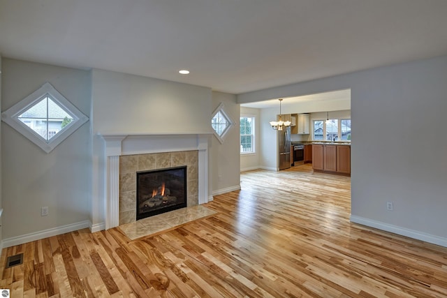 unfurnished living room with a chandelier, light wood-type flooring, sink, and a tiled fireplace