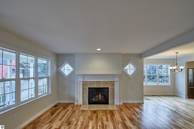 unfurnished living room featuring a fireplace, a chandelier, plenty of natural light, and light wood-type flooring