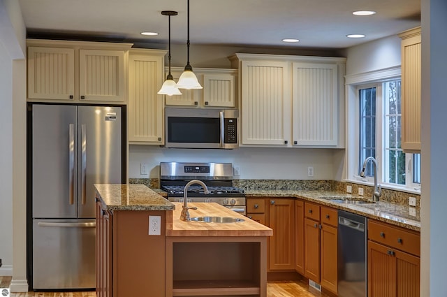 kitchen with pendant lighting, a kitchen island with sink, sink, appliances with stainless steel finishes, and butcher block countertops