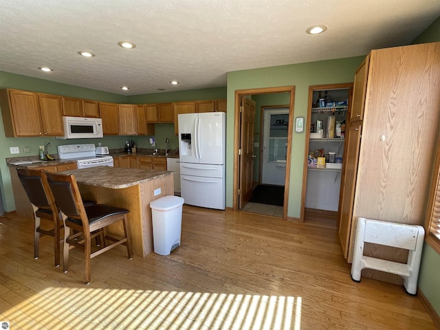 kitchen featuring white appliances, sink, a center island, light hardwood / wood-style floors, and a breakfast bar area