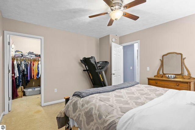 bedroom featuring a walk in closet, a closet, ceiling fan, and light colored carpet