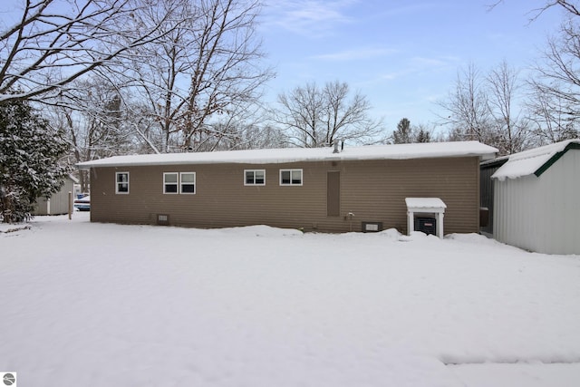 snow covered rear of property with a storage unit