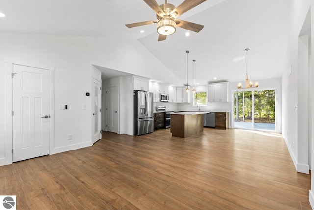 kitchen with ceiling fan with notable chandelier, stainless steel appliances, decorative light fixtures, white cabinets, and a kitchen island