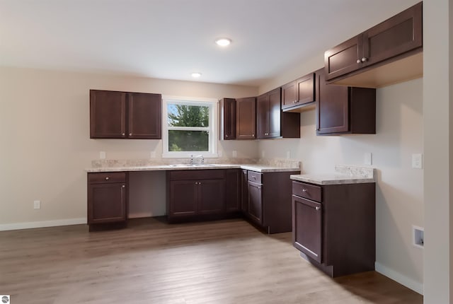 kitchen with light stone countertops, dark brown cabinetry, sink, and light hardwood / wood-style flooring