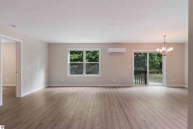 empty room with an AC wall unit, light wood-type flooring, and a notable chandelier