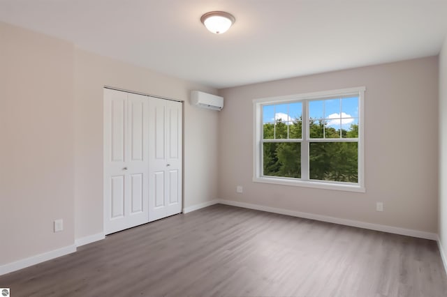 unfurnished bedroom with a wall mounted air conditioner, hardwood / wood-style flooring, and a closet