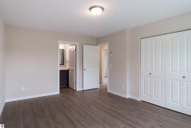 unfurnished bedroom with ensuite bath, a closet, and dark wood-type flooring