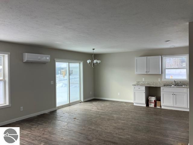 kitchen featuring pendant lighting, white cabinets, an AC wall unit, sink, and a notable chandelier