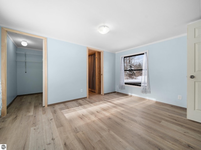 unfurnished bedroom with light wood-type flooring, a spacious closet, crown molding, and a closet