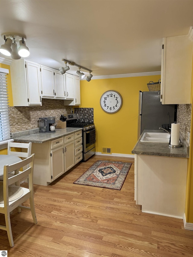 kitchen featuring white cabinetry, sink, stainless steel appliances, light hardwood / wood-style flooring, and backsplash