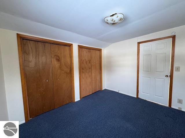 unfurnished bedroom with two closets, dark carpet, and lofted ceiling