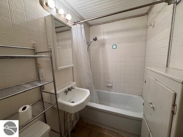 full bathroom with sink, shower / bath combination with curtain, tile walls, and toilet