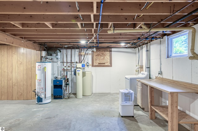 basement featuring washing machine and clothes dryer, wood walls, and gas water heater