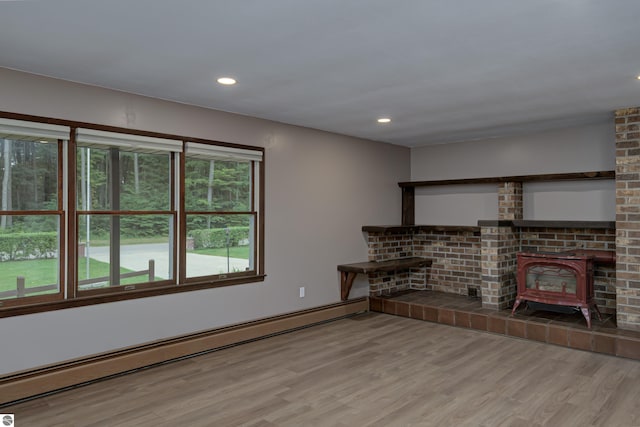 unfurnished living room featuring a wood stove, light hardwood / wood-style flooring, and a baseboard heating unit