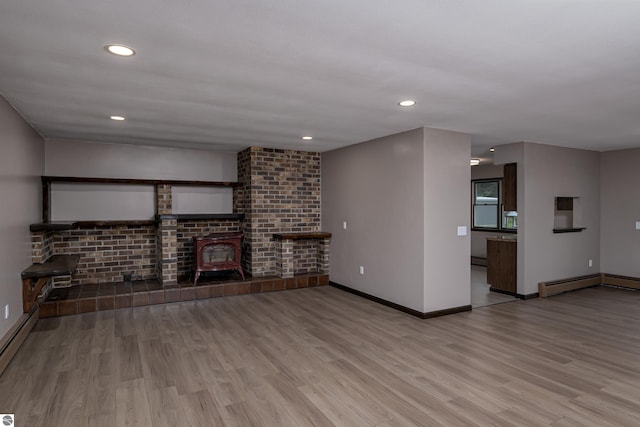 unfurnished living room featuring light wood-type flooring, a wood stove, and baseboard heating