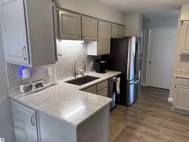 kitchen with stainless steel appliances, a peninsula, wood finished floors, a sink, and backsplash