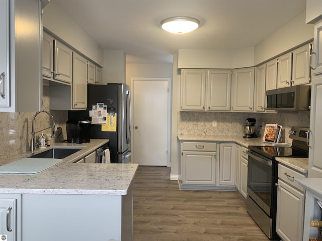 kitchen featuring a peninsula, a sink, wood finished floors, appliances with stainless steel finishes, and decorative backsplash