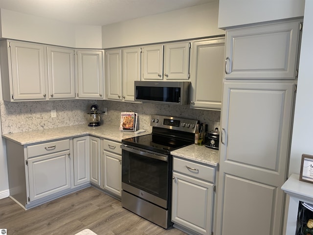 kitchen with light wood-style flooring, light stone counters, stainless steel appliances, and decorative backsplash