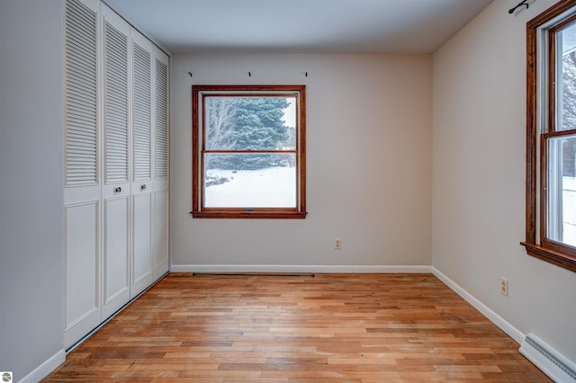 unfurnished bedroom with multiple windows, light hardwood / wood-style flooring, and a baseboard radiator