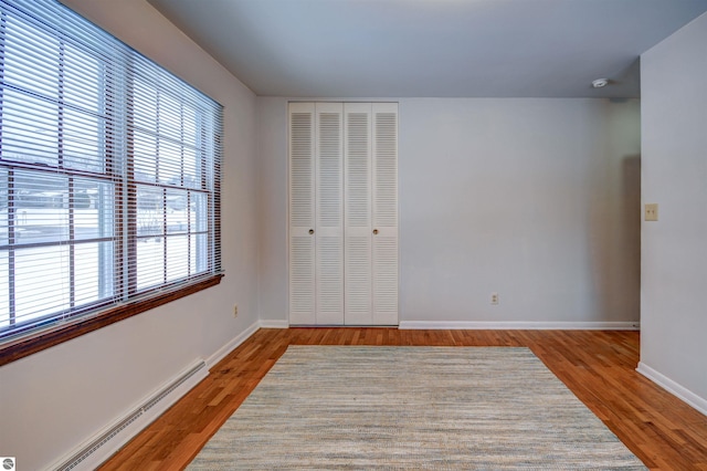 unfurnished bedroom with baseboard heating, multiple windows, and light hardwood / wood-style floors