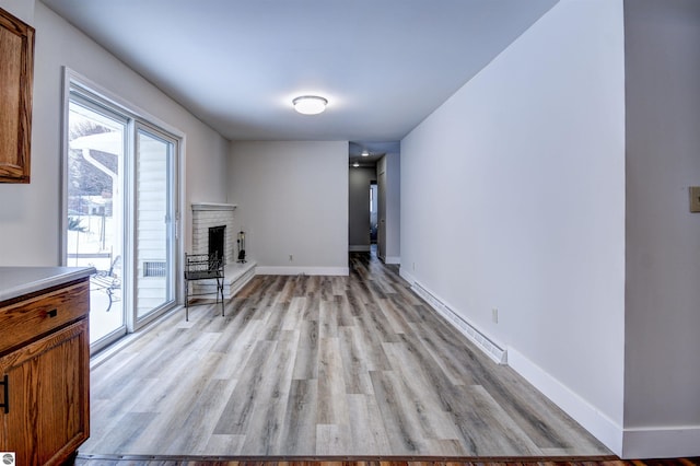 unfurnished living room featuring a baseboard radiator, a brick fireplace, and light hardwood / wood-style flooring