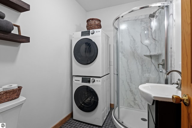 laundry area with dark tile patterned flooring and stacked washer / drying machine