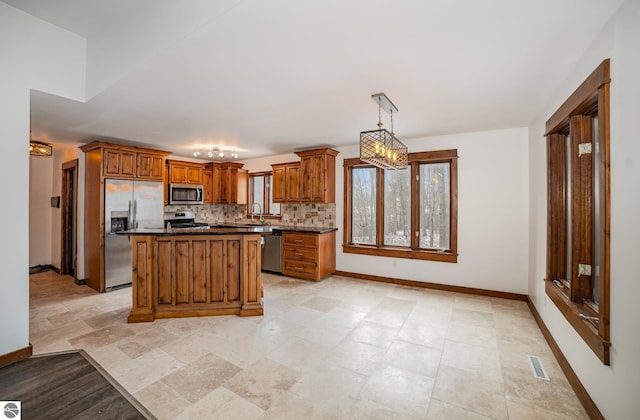 kitchen with appliances with stainless steel finishes, backsplash, a center island, hanging light fixtures, and sink