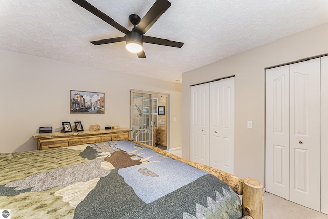 carpeted bedroom with a textured ceiling, ceiling fan, and two closets