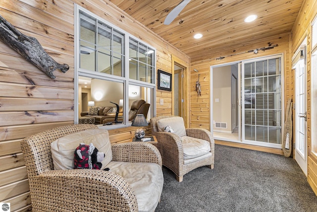 sitting room with carpet, ceiling fan, wooden ceiling, and wooden walls