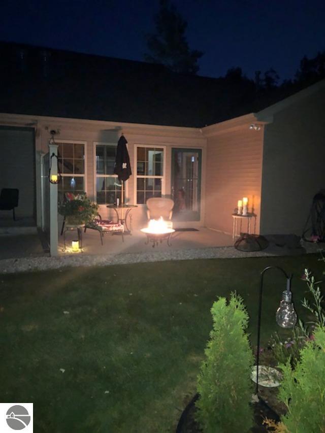 back house at night featuring a lawn and a patio area