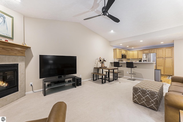 carpeted living room featuring a tiled fireplace, ceiling fan, and lofted ceiling