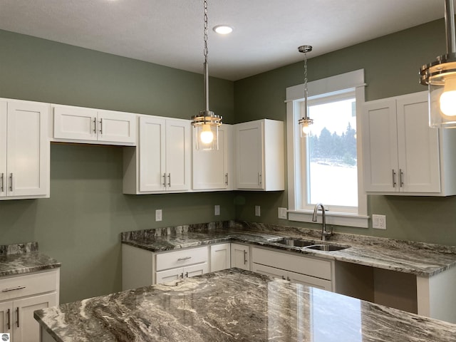 kitchen featuring white cabinets, decorative light fixtures, sink, and dark stone counters