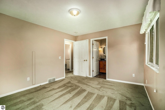 unfurnished bedroom with dark colored carpet and ensuite bathroom