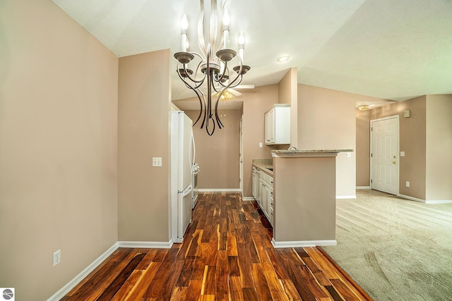 kitchen featuring lofted ceiling, an inviting chandelier, white cabinets, white fridge, and light stone counters