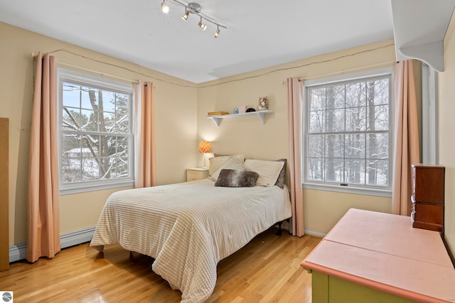 bedroom featuring light wood-type flooring, track lighting, and a baseboard heating unit