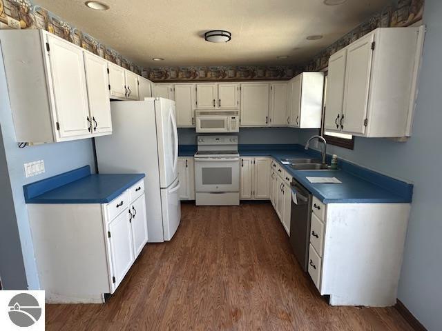 kitchen featuring white appliances, white cabinetry, dark wood-type flooring, and sink