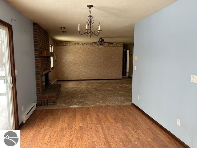 interior space featuring a brick fireplace, wood-type flooring, a chandelier, and a baseboard heating unit