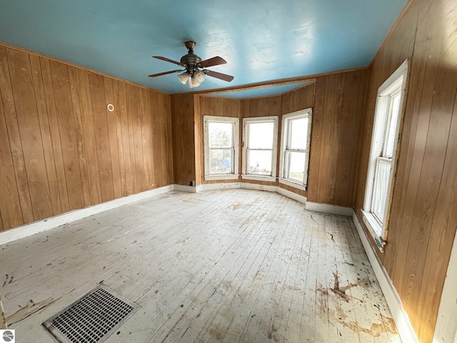 spare room with ceiling fan, light hardwood / wood-style flooring, and wood walls