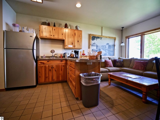 kitchen with pendant lighting, light tile patterned floors, stainless steel counters, kitchen peninsula, and stainless steel refrigerator