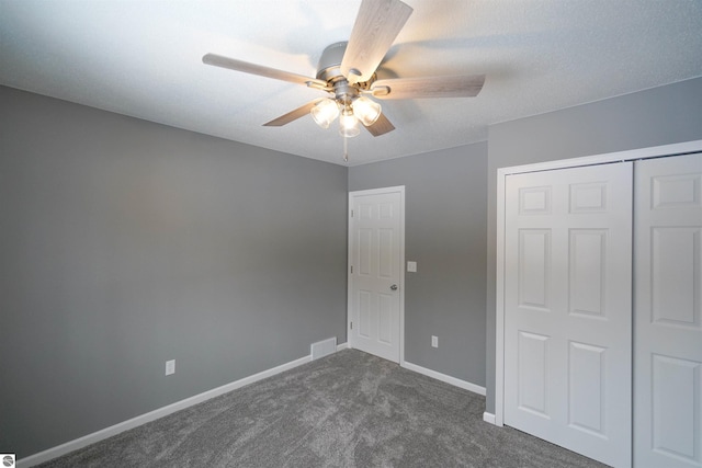 unfurnished bedroom with dark colored carpet, a closet, and ceiling fan