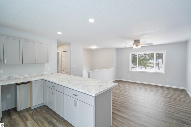 kitchen with light stone countertops, ceiling fan, dark wood-type flooring, kitchen peninsula, and a textured ceiling