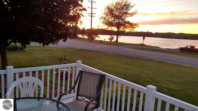 deck at dusk with a water view and a yard