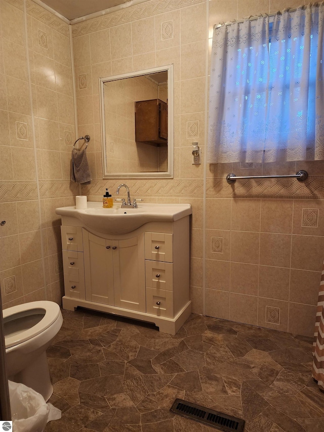 bathroom featuring vanity, toilet, and tile walls