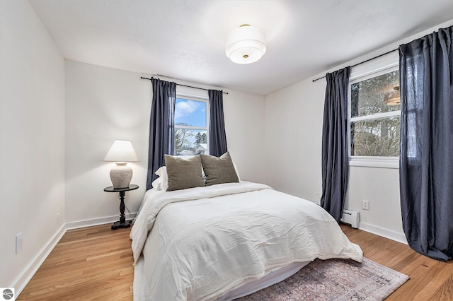 bedroom with light hardwood / wood-style floors and a baseboard heating unit