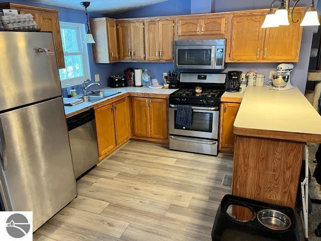 kitchen featuring sink, stainless steel appliances, kitchen peninsula, light hardwood / wood-style floors, and decorative light fixtures