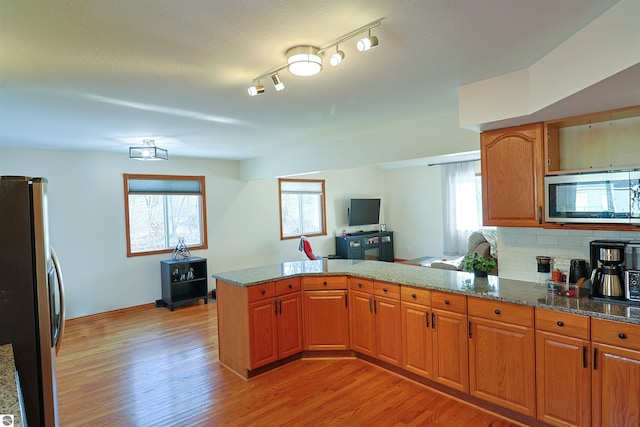 kitchen with decorative backsplash, dark stone countertops, light hardwood / wood-style floors, kitchen peninsula, and stainless steel appliances