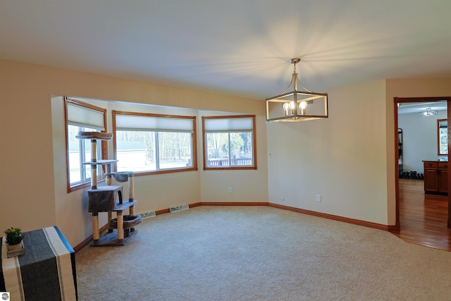 carpeted empty room featuring a healthy amount of sunlight and a notable chandelier